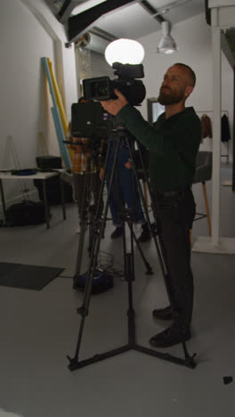 Vertical-Video-Of-Male-Film-Camera-Operator-Shooting-Movie-Or-Video-In-Studio-Using-Tripod-1